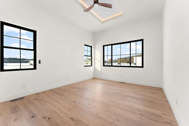 an empty room with wooden floor ceiling fan and windows