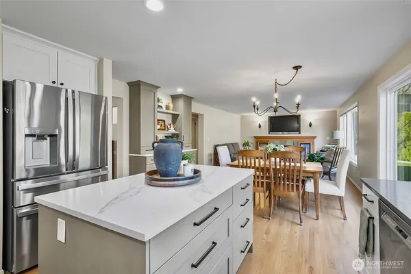 a kitchen with stainless steel appliances kitchen island granite countertop a refrigerator a stove top oven a dining table and chairs with wooden floor