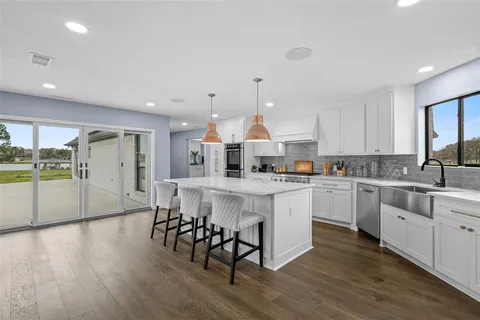 a kitchen with stainless steel appliances granite countertop a stove a sink a refrigerator and white cabinets with wooden floor