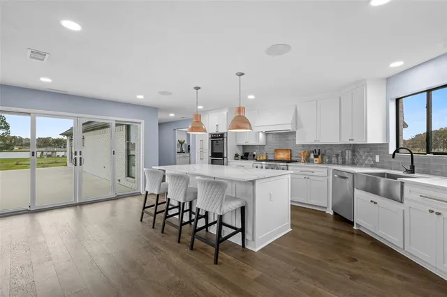 a kitchen with stainless steel appliances granite countertop a stove a sink a refrigerator and white cabinets with wooden floor