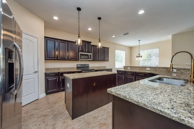 a kitchen with kitchen island granite countertop stainless steel appliances cabinets a sink and a counter top space