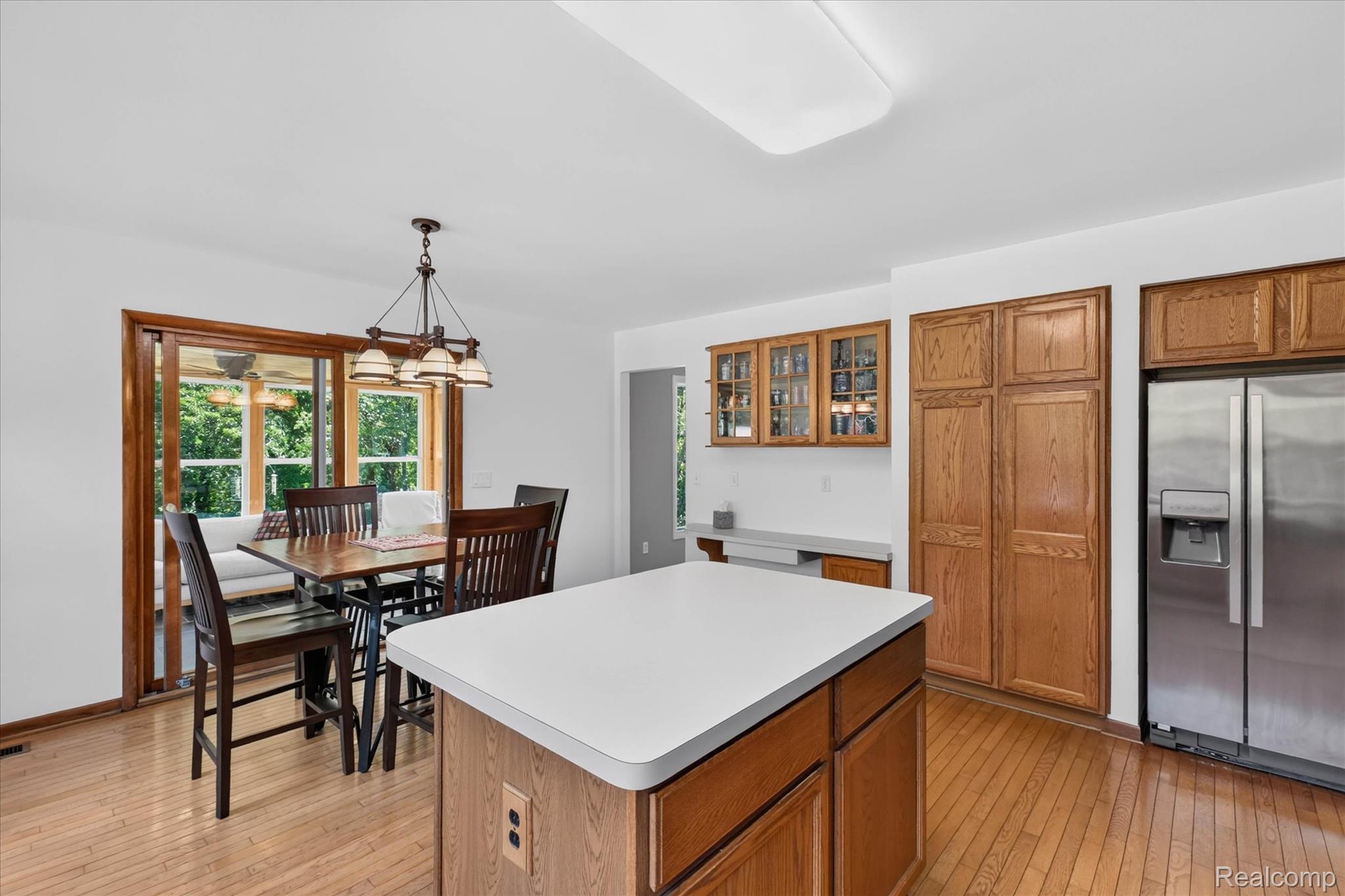 4037 Chilson Road Howell, MI 48843 - Photo 9 of 69 Wood-finish flooring, central island with solid surface countertop, built-in oak cabinetry, stainless steel refrigerator, and glass-paneled sliding door