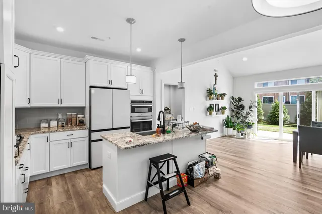 a kitchen with stainless steel appliances kitchen island granite countertop a refrigerator a stove a sink dishwasher and white cabinets with wooden floor