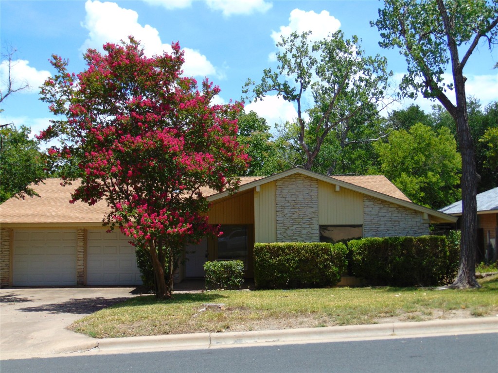 View of front of property with stone siding, concrete driveway, and roof with shingles