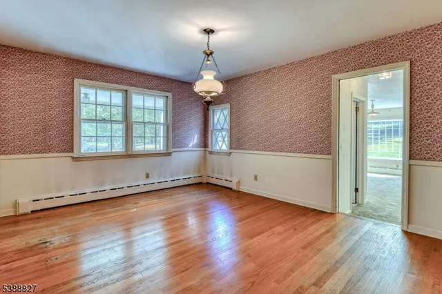an empty room with wooden floor chandelier and windows