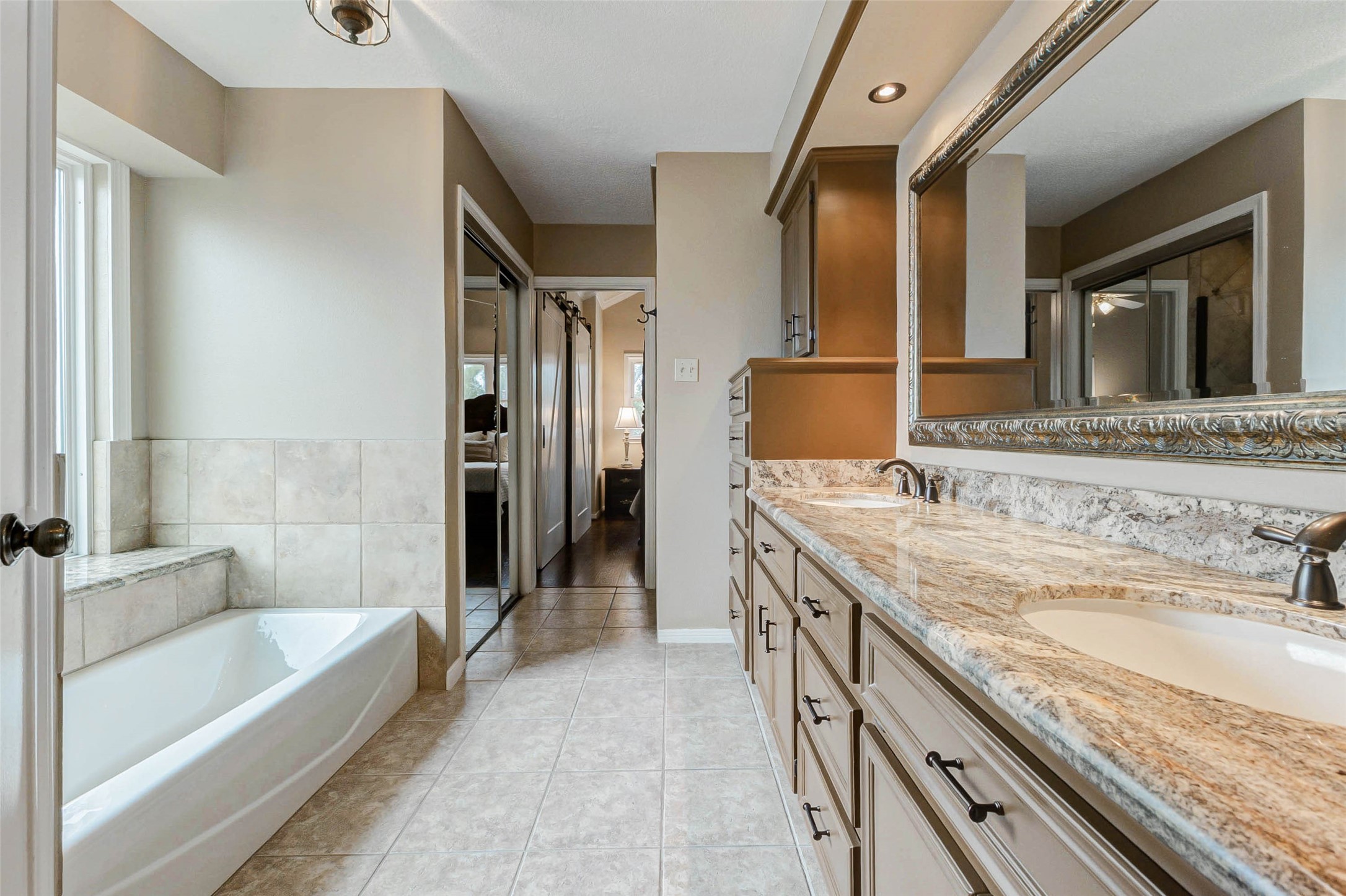 15811 Spring Forest Drive Houston, TX 77059 - Photo 21 of 27 This bathroom features a spacious layout with a large vanity and dual sinks, a luxurious soaking tub, and elegant tile flooring. Natural light enhances the neutral tones, creating a serene and inviting atmosphere.