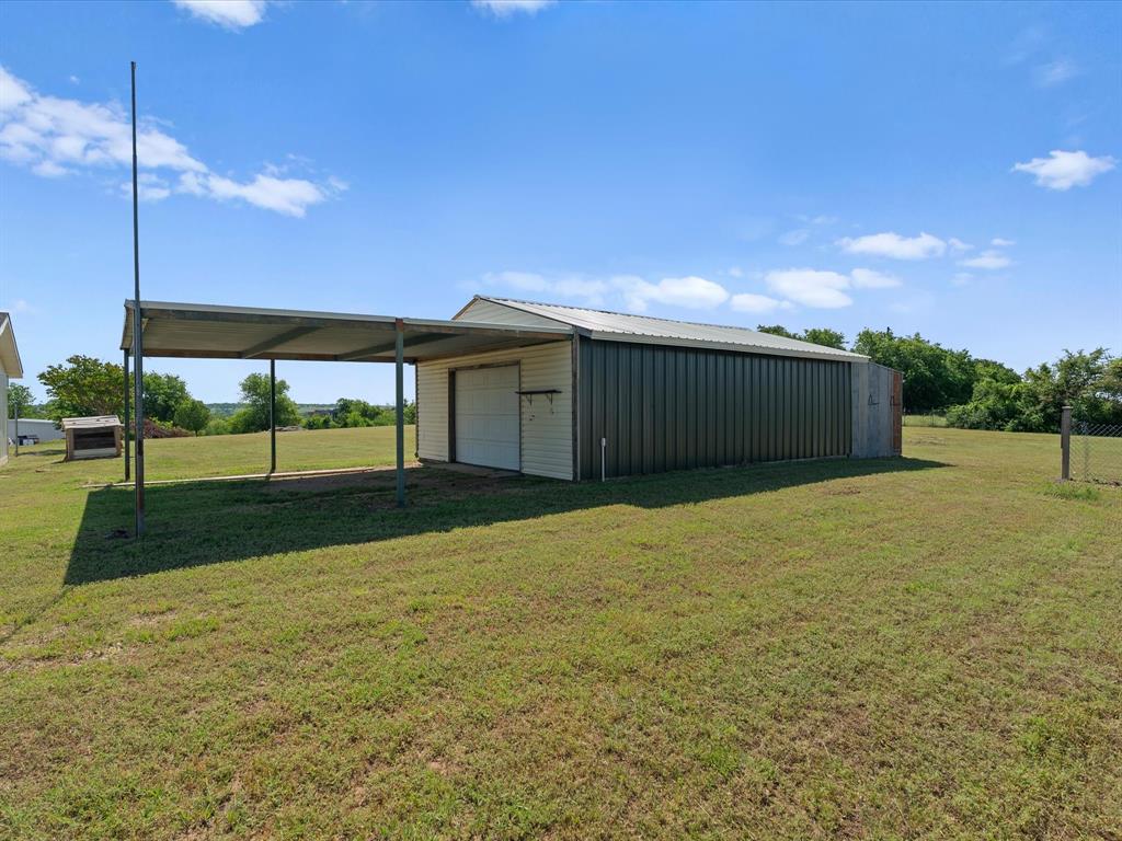 289 County Road 4655 Rhome, TX 76078 - Photo 26 of 34 Metal outbuilding with a carport, featuring a roll-up garage door and an additional side entry