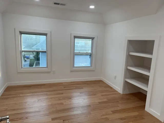 a view of an empty room with a window and wooden floor