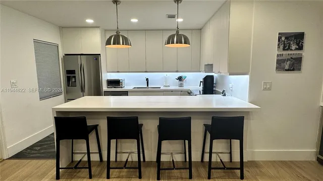 a kitchen with stainless steel appliances kitchen island granite countertop a dining table chairs and a refrigerator
