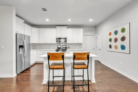 a kitchen with stainless steel appliances granite countertop a dining table chairs refrigerator and sink