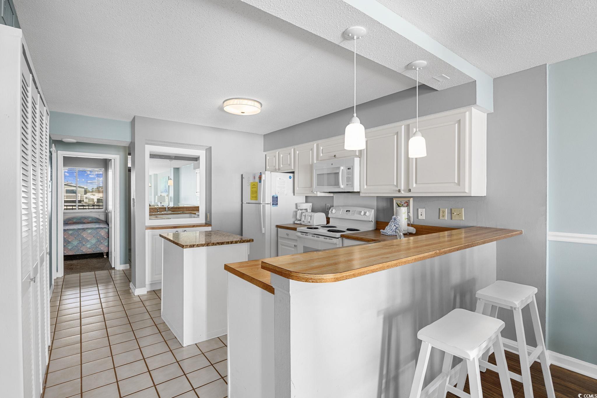 4701 South Ocean Boulevard, Unit 2B North Myrtle Beach, SC 29582 - Photo 4 of 31 Kitchen with a peninsula, pendant lighting, white cabinets, white appliances, and a kitchen island