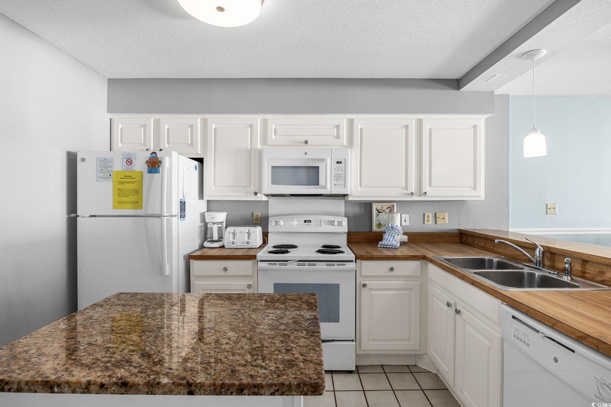 4701 South Ocean Boulevard, Unit 2B North Myrtle Beach, SC 29582 - Photo 5 of 31 Kitchen featuring white appliances, white cabinets, light tile patterned flooring, hanging light fixtures, and a textured ceiling