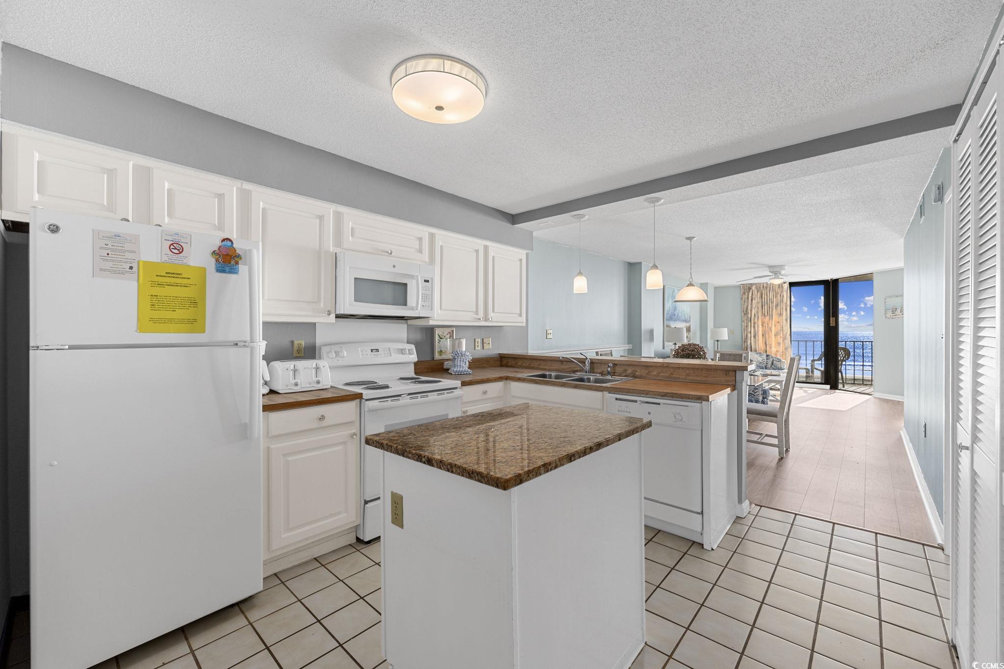 4701 South Ocean Boulevard, Unit 2B North Myrtle Beach, SC 29582 - Photo 6 of 31 Kitchen with white appliances, a textured ceiling, light tile patterned floors, white cabinets, and pendant lighting