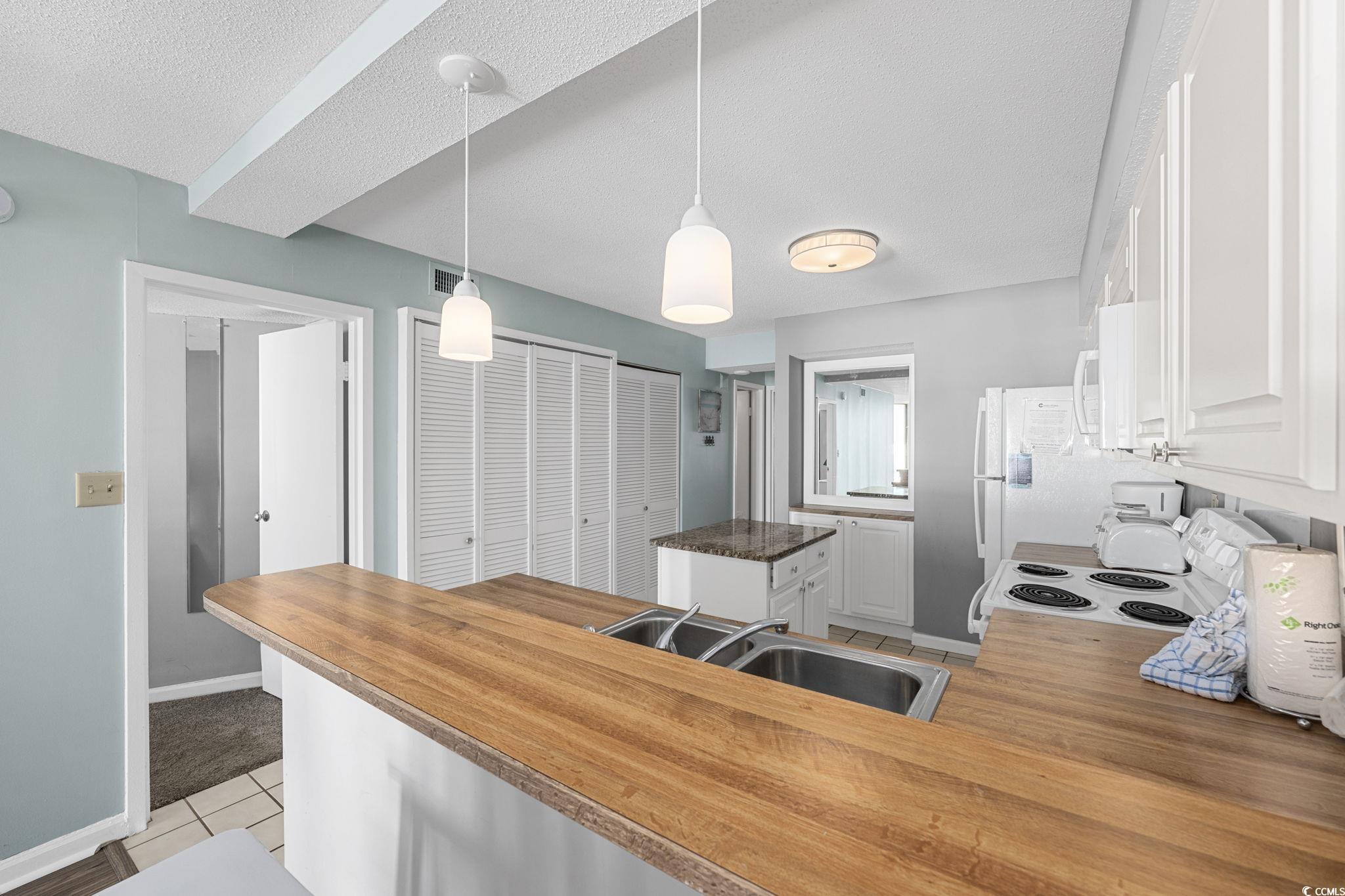 4701 South Ocean Boulevard, Unit 2B North Myrtle Beach, SC 29582 - Photo 7 of 31 Kitchen with white cabinetry, pendant lighting, light tile patterned floors, white appliances, and a textured ceiling