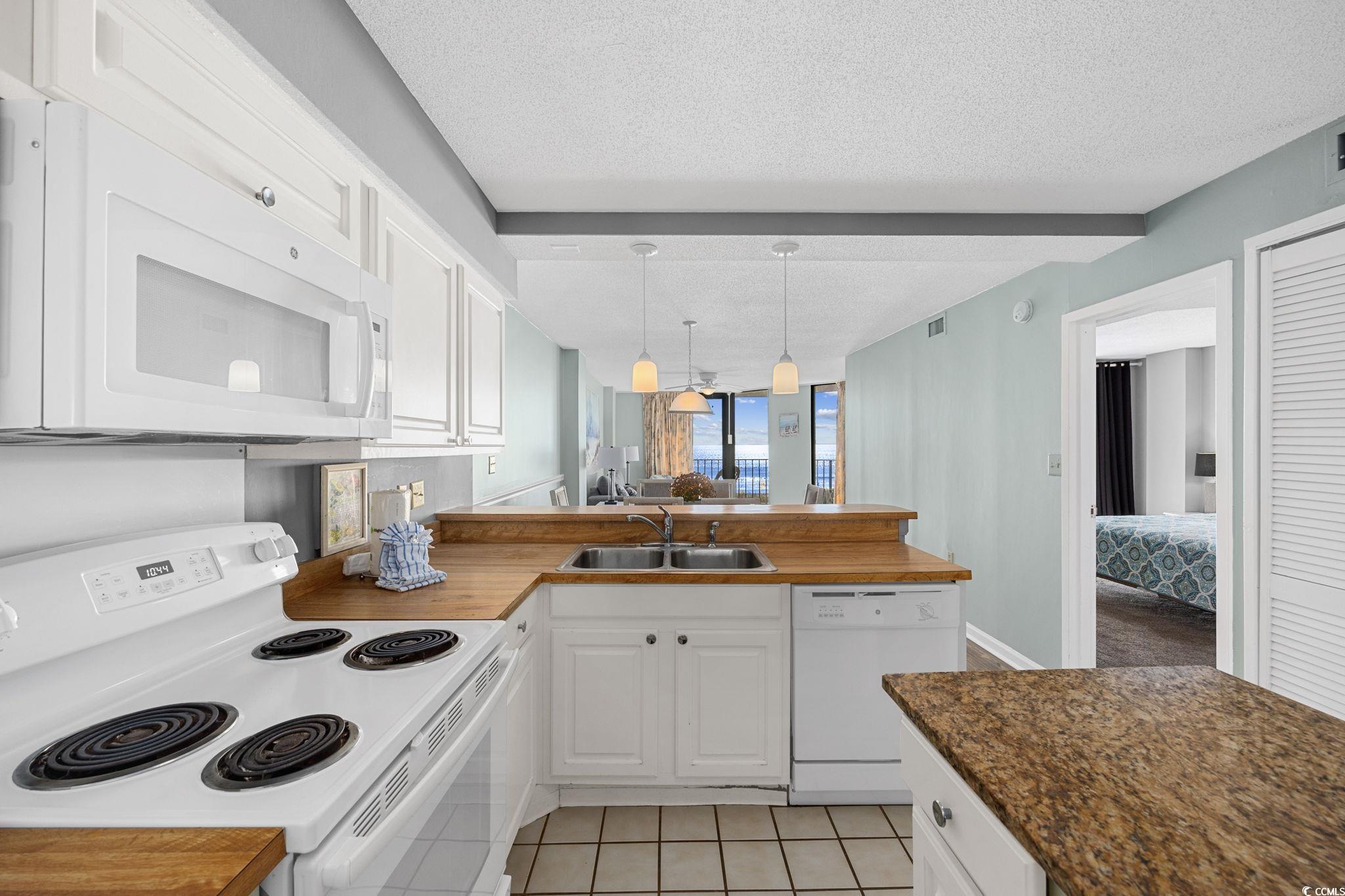 4701 South Ocean Boulevard, Unit 2B North Myrtle Beach, SC 29582 - Photo 8 of 31 Kitchen with white appliances, white cabinets, a textured ceiling, decorative light fixtures, and light tile patterned flooring