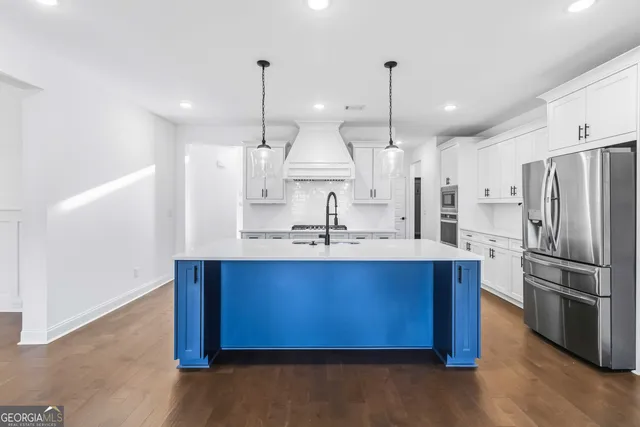 a large kitchen with stainless steel appliances kitchen island granite countertop a sink a refrigerator and a wooden floor