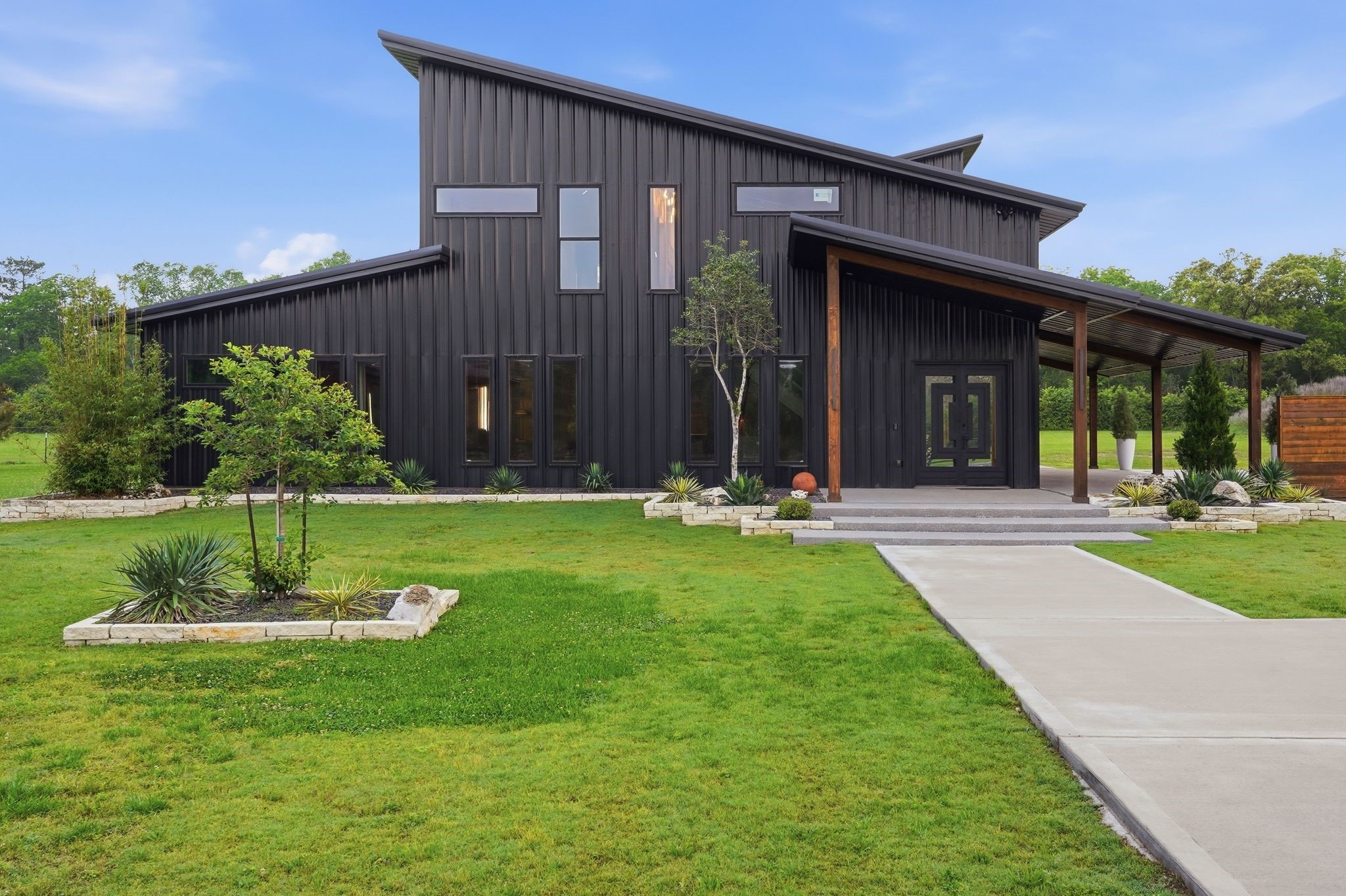 2743 Bobville Road Montgomery, TX 77316 - Photo 15 of 50 This modern home features a sleek, angular design with a dark exterior. It has large windows for natural light and a spacious covered entryway. The well-maintained lawn and minimalist landscaping add to its contemporary appeal.