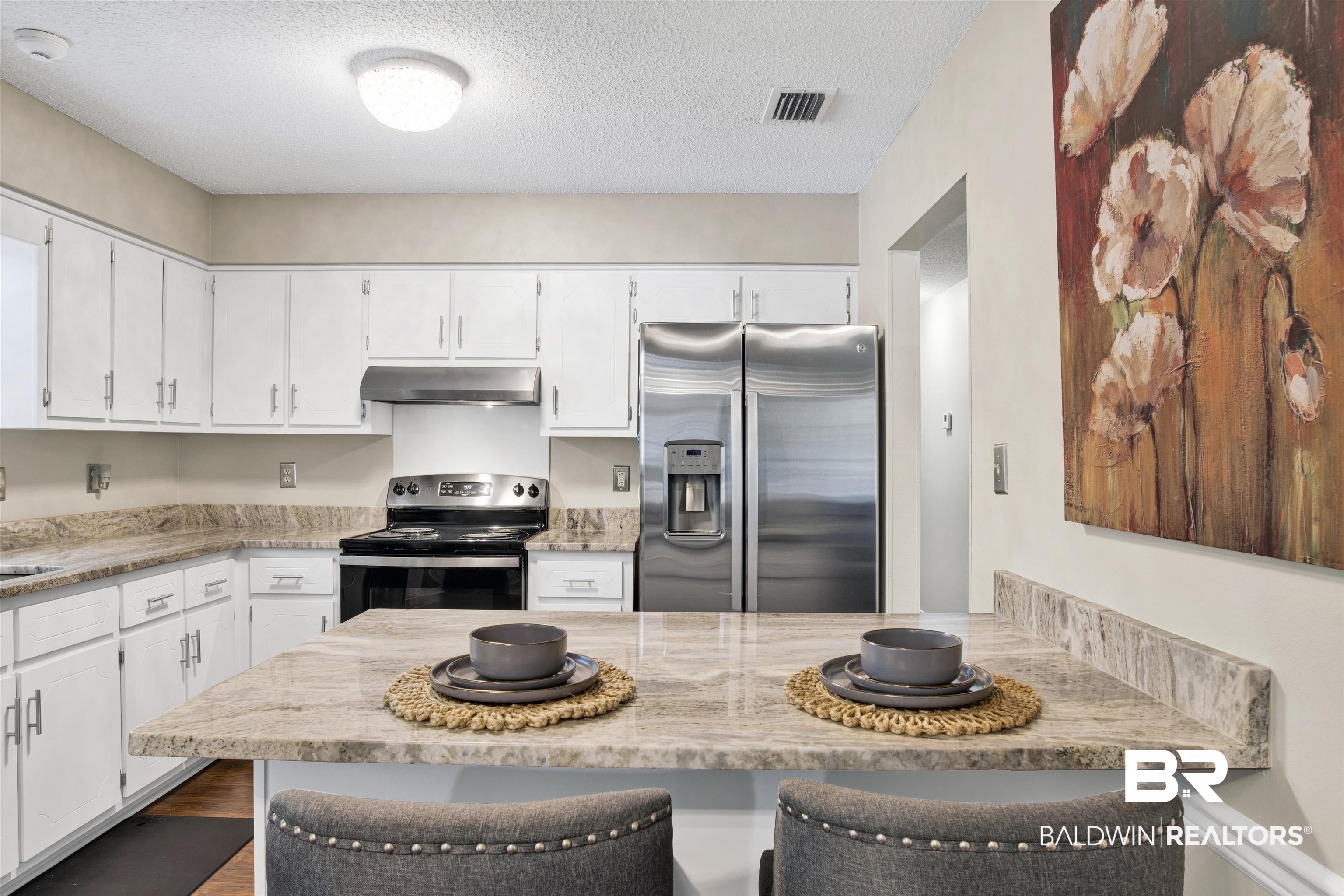 6281 Woodside Drive Theodore, AL 36582 - Photo 7 of 17 Kitchen featuring stainless steel appliances, a textured ceiling, white cabinets, under cabinet range hood, and a breakfast bar area