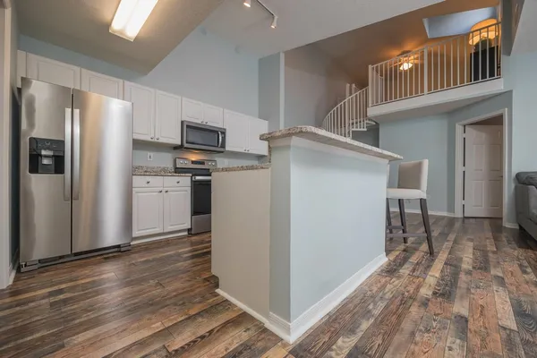 a kitchen with stainless steel appliances granite countertop a refrigerator a stove and a sink with wooden floors