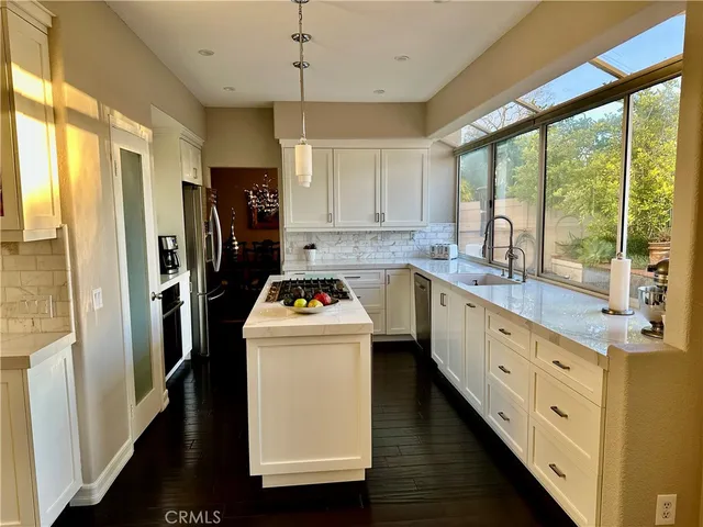 a kitchen with stainless steel appliances a stove a refrigerator a sink and white cabinets with wooden floor