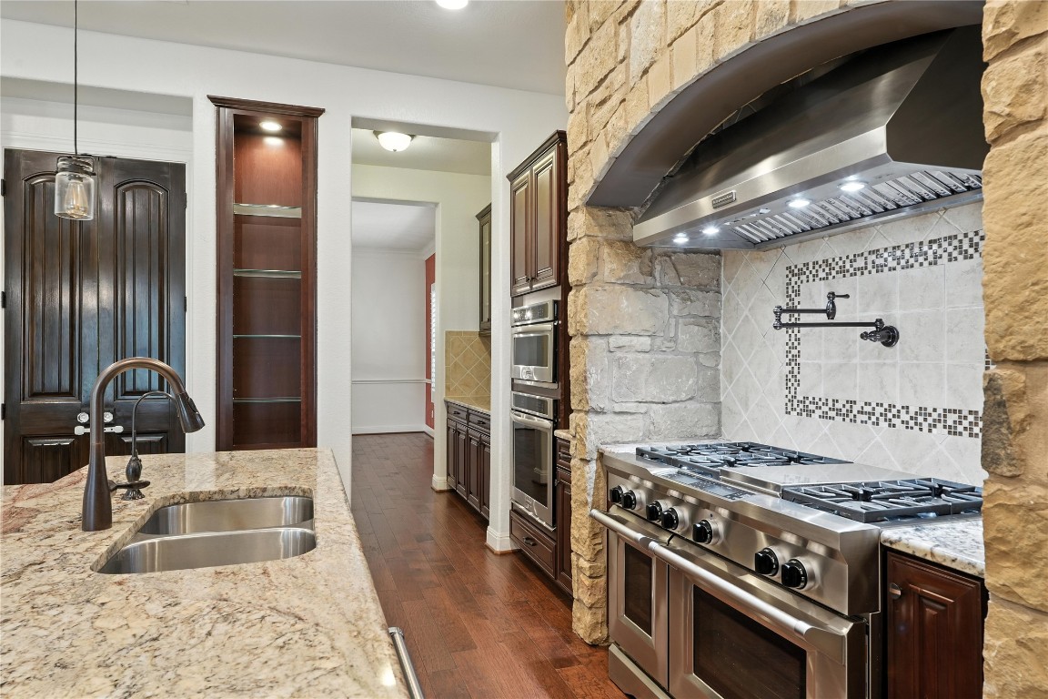 15729 De Fortuna Drive Bee Cave, TX 78738 - Photo 12 of 40 Kitchen with wall chimney range hood, double oven range, light stone counters, and dark wood-style floors
