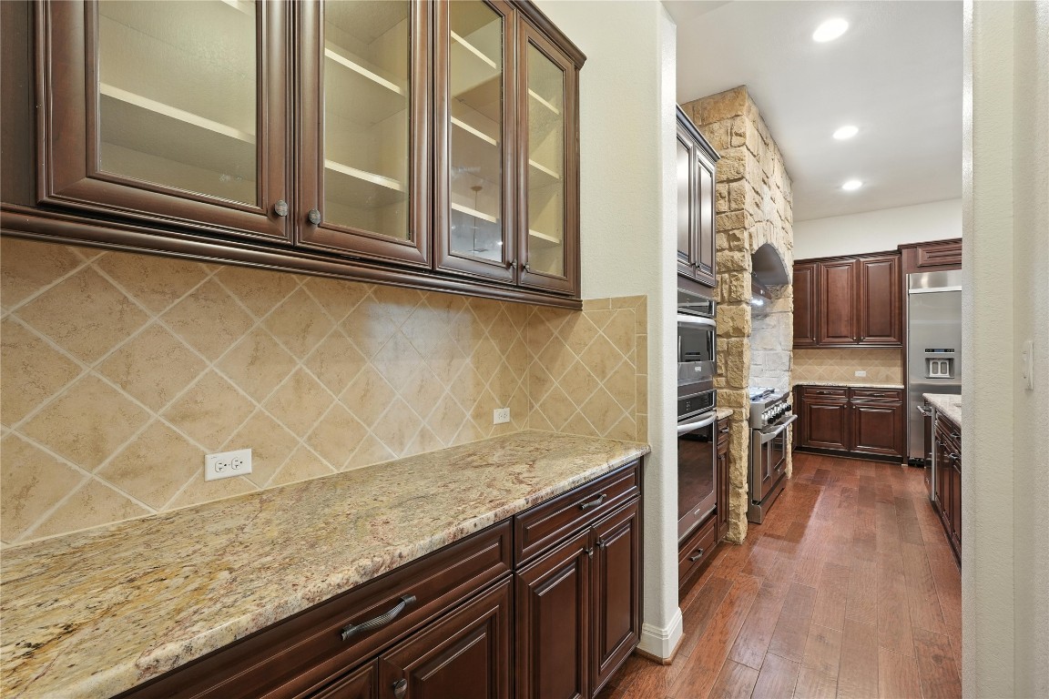 15729 De Fortuna Drive Bee Cave, TX 78738 - Photo 14 of 40 Kitchen with decorative backsplash, dark wood-type flooring, light stone countertops, glass insert cabinets, and recessed lighting