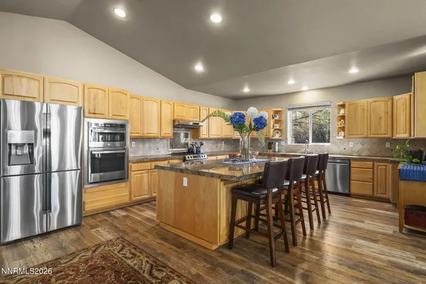 a kitchen with stainless steel appliances kitchen island granite countertop a refrigerator a stove a sink a dining table and chairs with wooden floor