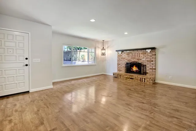 an empty room with wooden floor fireplace and windows