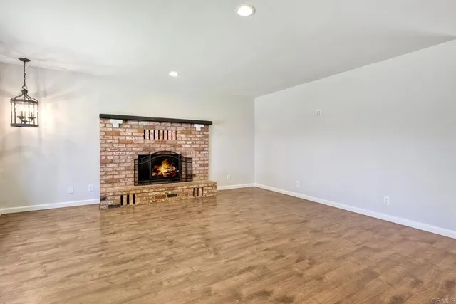 a view of an empty room with wooden floor fireplace and a window