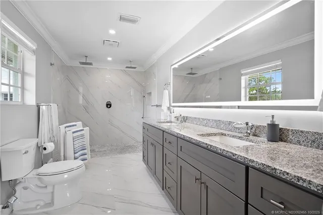 a spacious bathroom with a granite countertop double vanity sink a mirror and a toilet