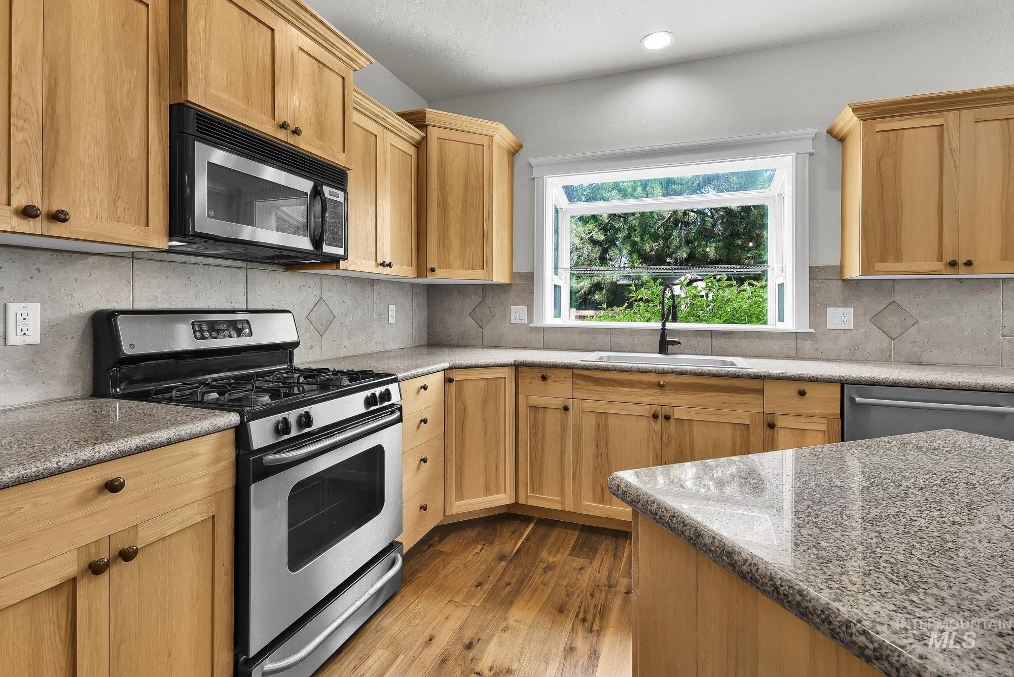 2172 West Cedar Grove Street Meridian, ID 83646 - Photo 11 of 49 Kitchen featuring light wood cabinetry, stone-finish countertops, stainless steel appliances, and wood-finish flooring