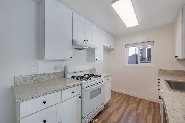 a kitchen with granite countertop a stove a sink and white cabinets with wooden floor