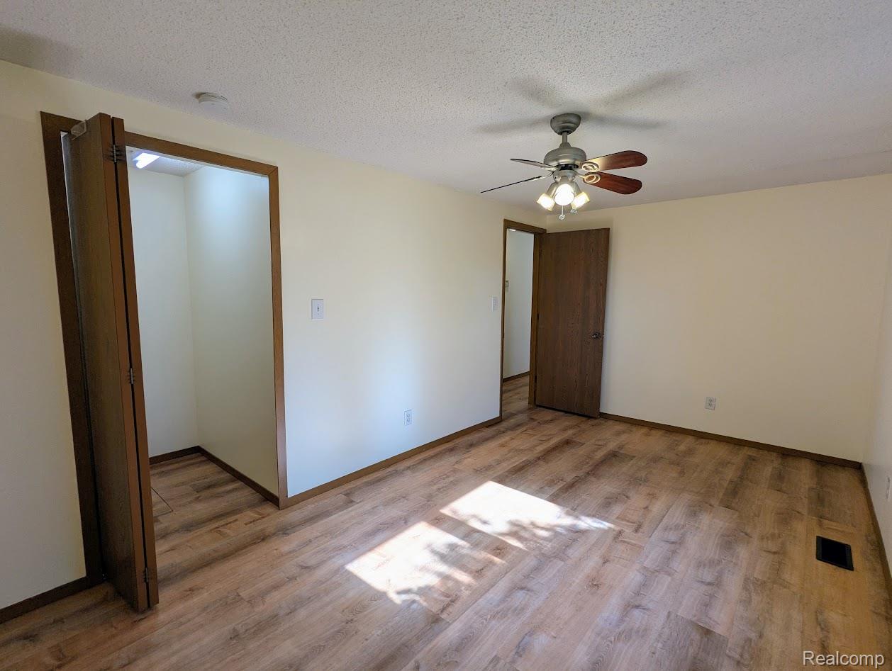 2316 Crescent Lake Road Waterford, MI 48329 - Photo 11 of 17 Spacious interior room featuring wood-finish flooring, light-colored walls, a ceiling fan with integrated lighting, and dark wood trim