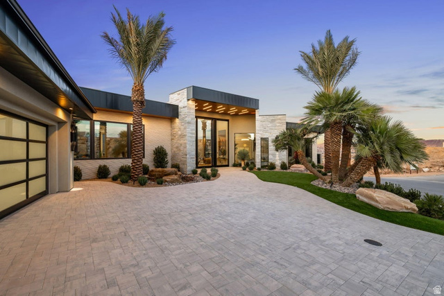 2867 East Granite Way St. George, UT 84790 - Photo 66 of 69 Contemporary exterior featuring a stone facade, a multi-pane glass garage door, a paver driveway, mature palm trees, and manicured landscaping