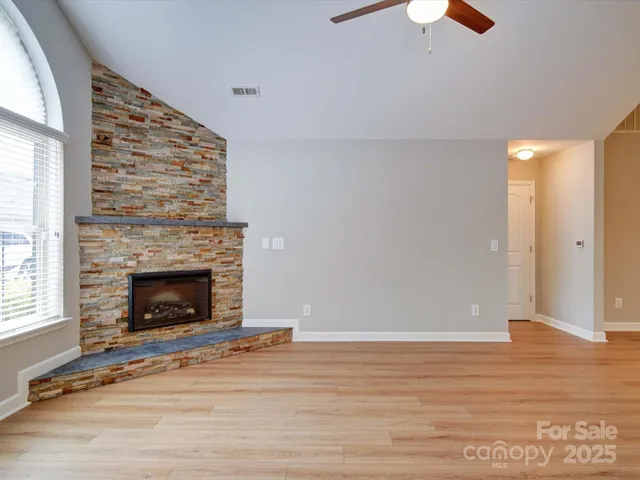 a view of an empty room with wooden floor fireplace and a window
