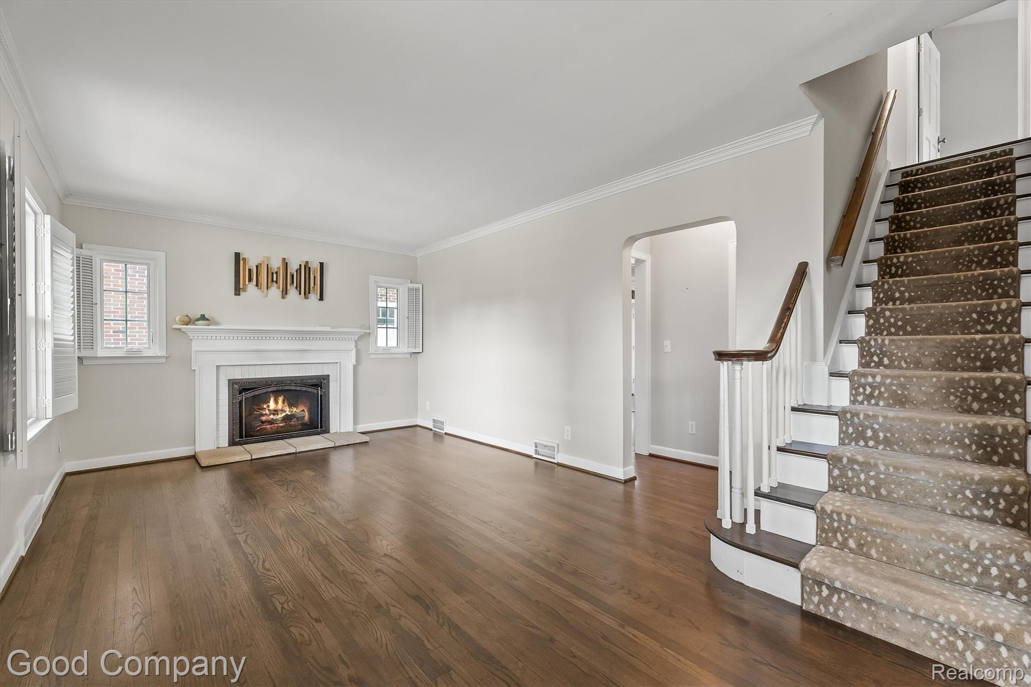 317 Wesley Street Rochester, MI 48307 - Photo 4 of 29 Unfurnished living room with arched walkways, crown molding, dark wood-style floors, and a warm lit fireplace