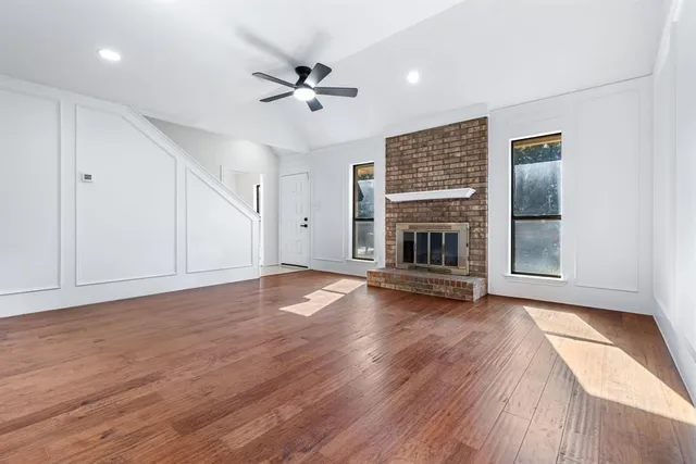 a view of an empty room with wooden floor fireplace and a window