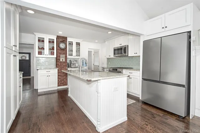 a kitchen with stainless steel appliances granite countertop a refrigerator a stove a sink and white cabinets with wooden floor