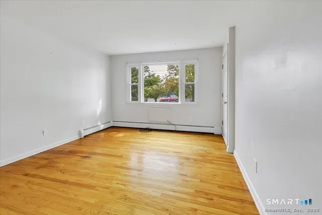 a view of an empty room with wooden floor and a window