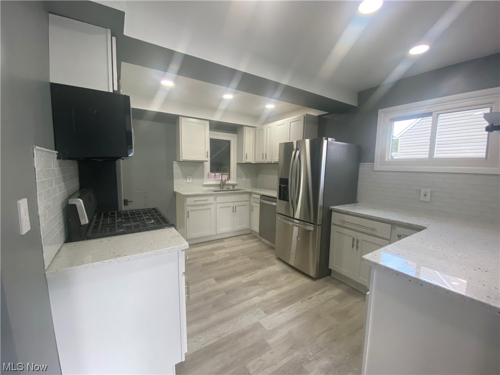 12913 Silver Road Cleveland, OH 44125 - Photo 6 of 23 Kitchen featuring backsplash, white cabinets, light countertops, light hardwood flooring, and stainless steel appliances