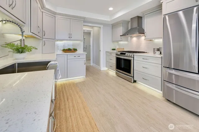 a kitchen with granite countertop a refrigerator oven a sink dishwasher and white cabinets with wooden floor