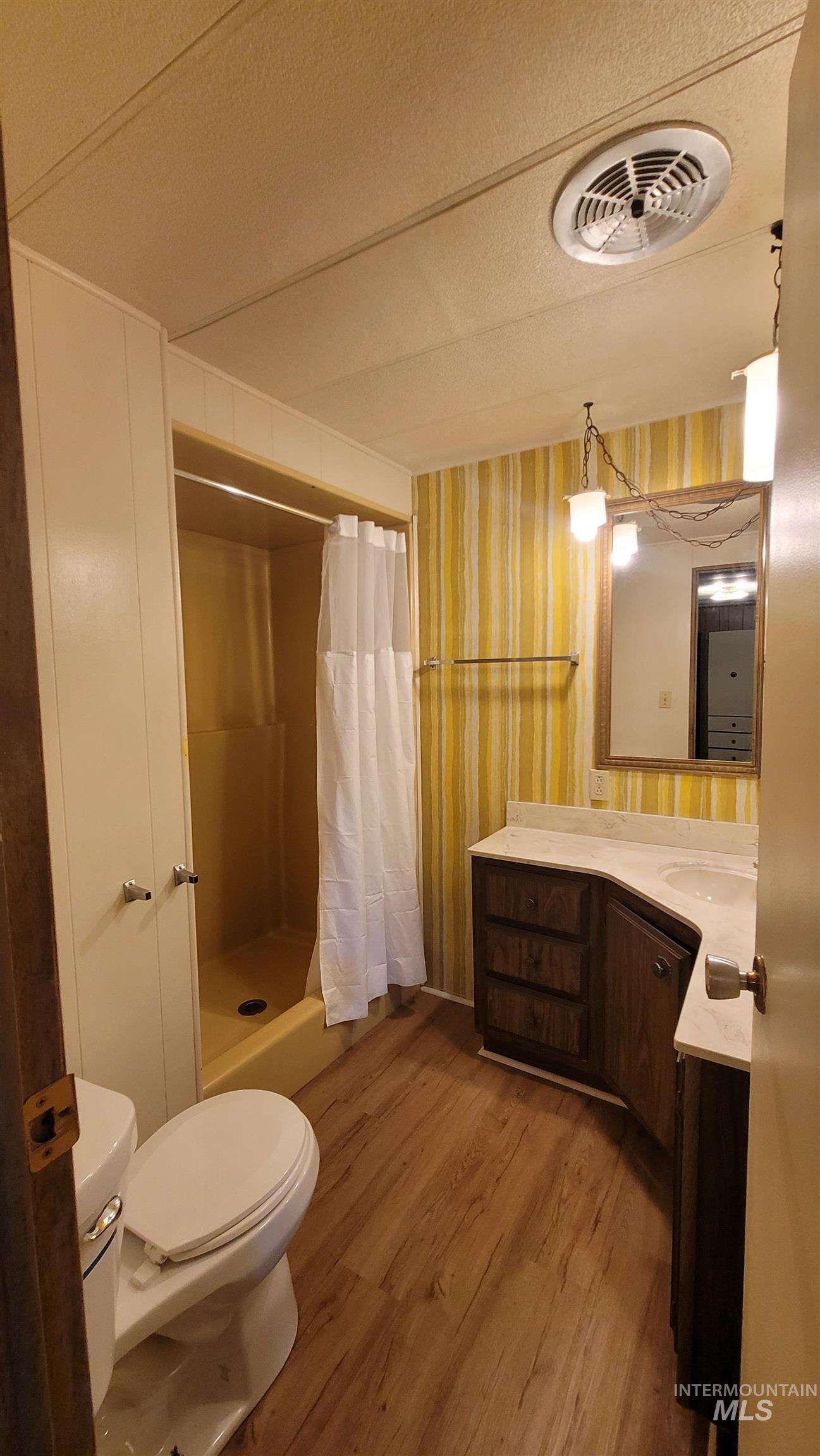 2122 Highway 95 Council, ID 83612 - Photo 16 of 31 Full bathroom featuring vanity, a shower stall, a textured ceiling, light wood-style floors, and wallpapered walls
