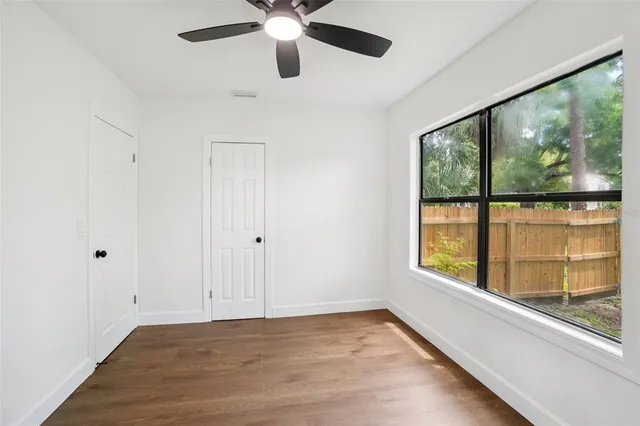 an empty room with wooden floor fan and windows