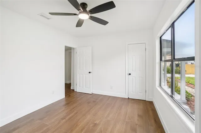 an empty room with wooden floor ceiling fan and windows