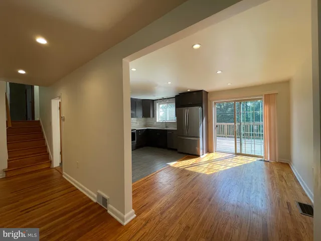 a view of an empty room with wooden floor and a kitchen
