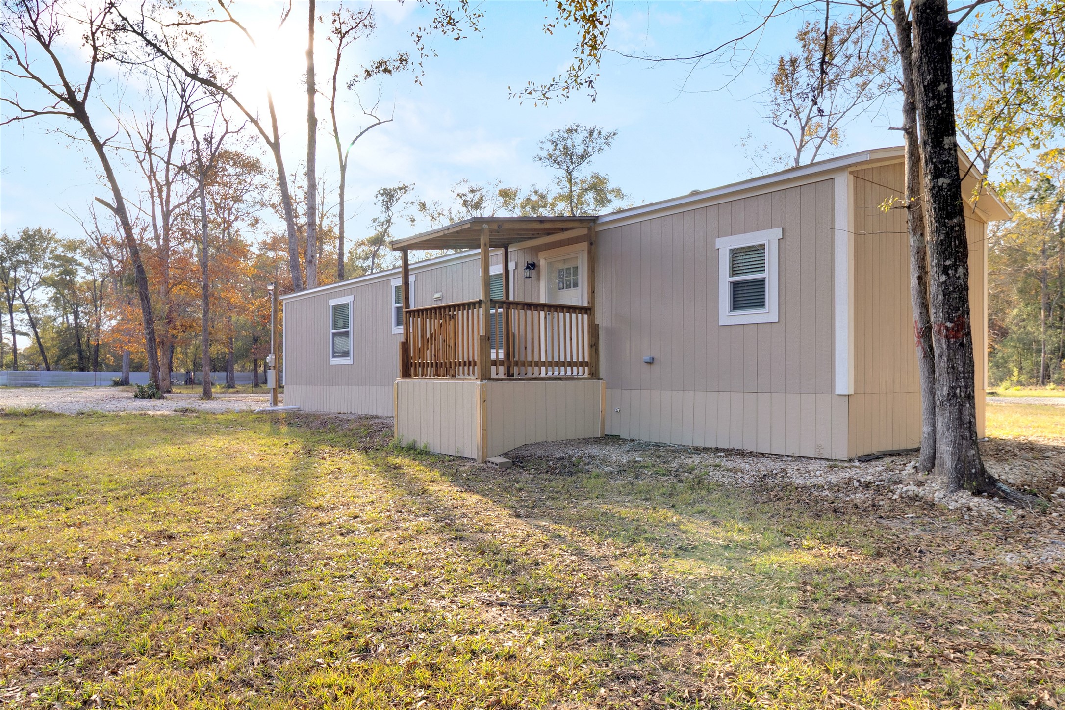 This photo showcases a mobile home with a small front porch, set on a spacious, grassy lot surrounded by trees. The exterior is neutral-toned, blending well with the natural setting, offering a peaceful, rural atmosphere.