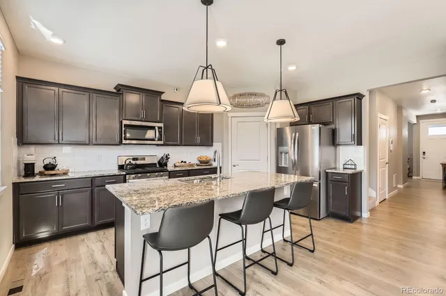 a kitchen with stainless steel appliances kitchen island granite countertop a sink a stove a refrigerator and island with wooden floor