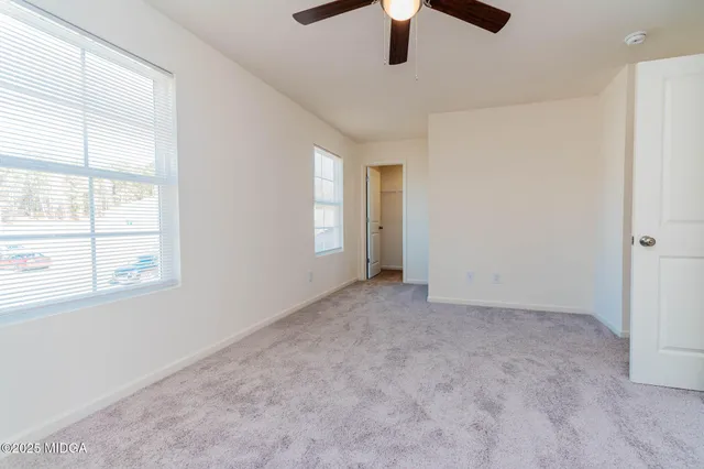 an empty room with chandelier fan and windows