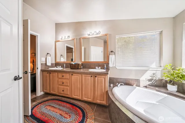 a spacious bathroom with a double vanity sink a mirror a bathtub and next to a window