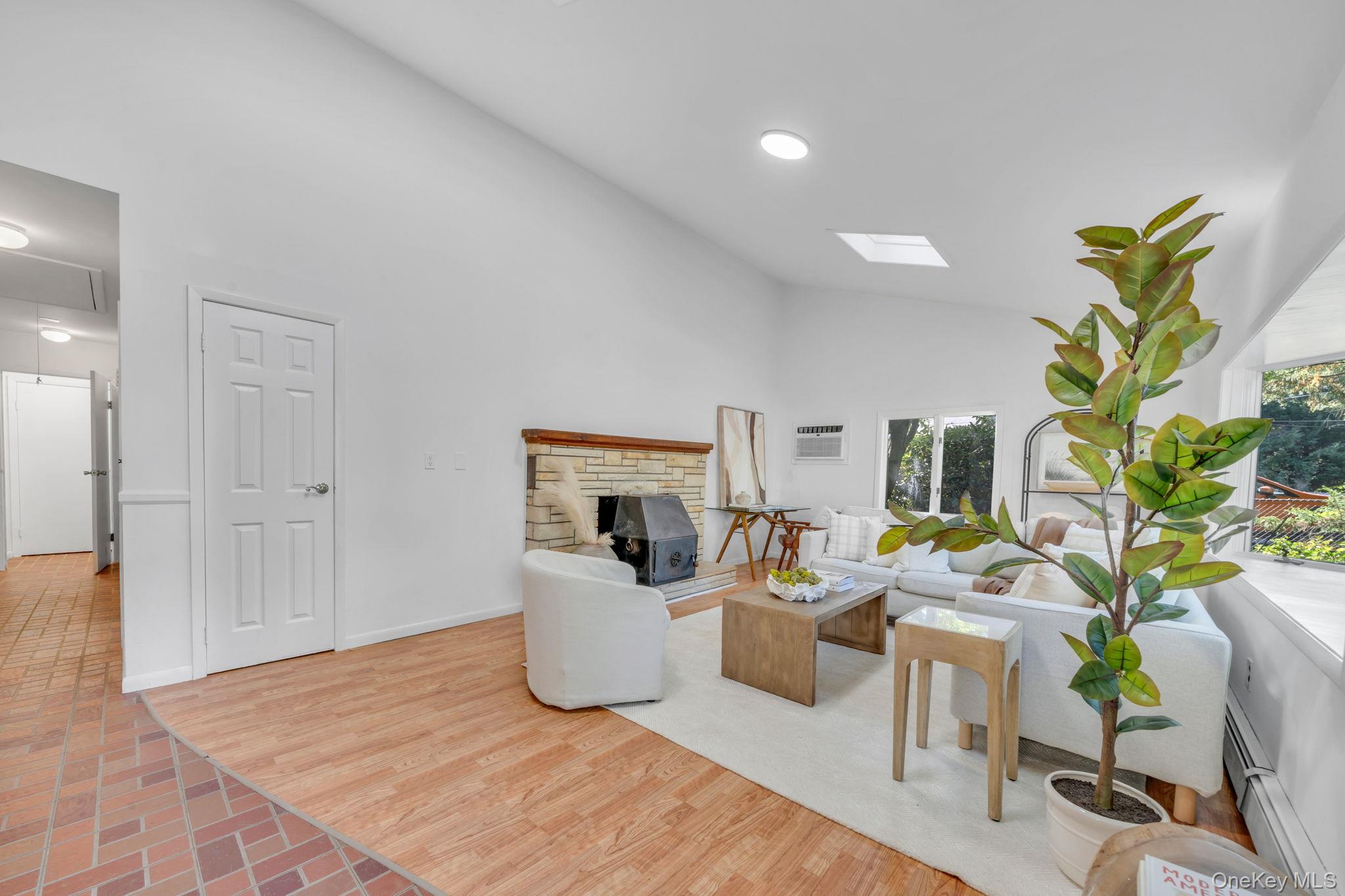 60 Hawthorne Road Rocky Point, NY 11778 - Photo 2 of 23 Living room featuring high vaulted ceiling, baseboard heating, attic access, light wood-style flooring, and a skylight